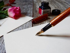 pennsa stilografica e inchiostro, foglio idi carta e una rosa