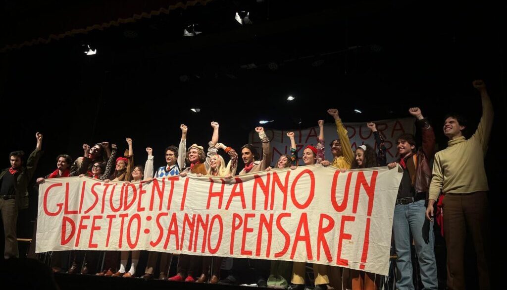 Il cast è in scena esibendo uno striscione di protesta