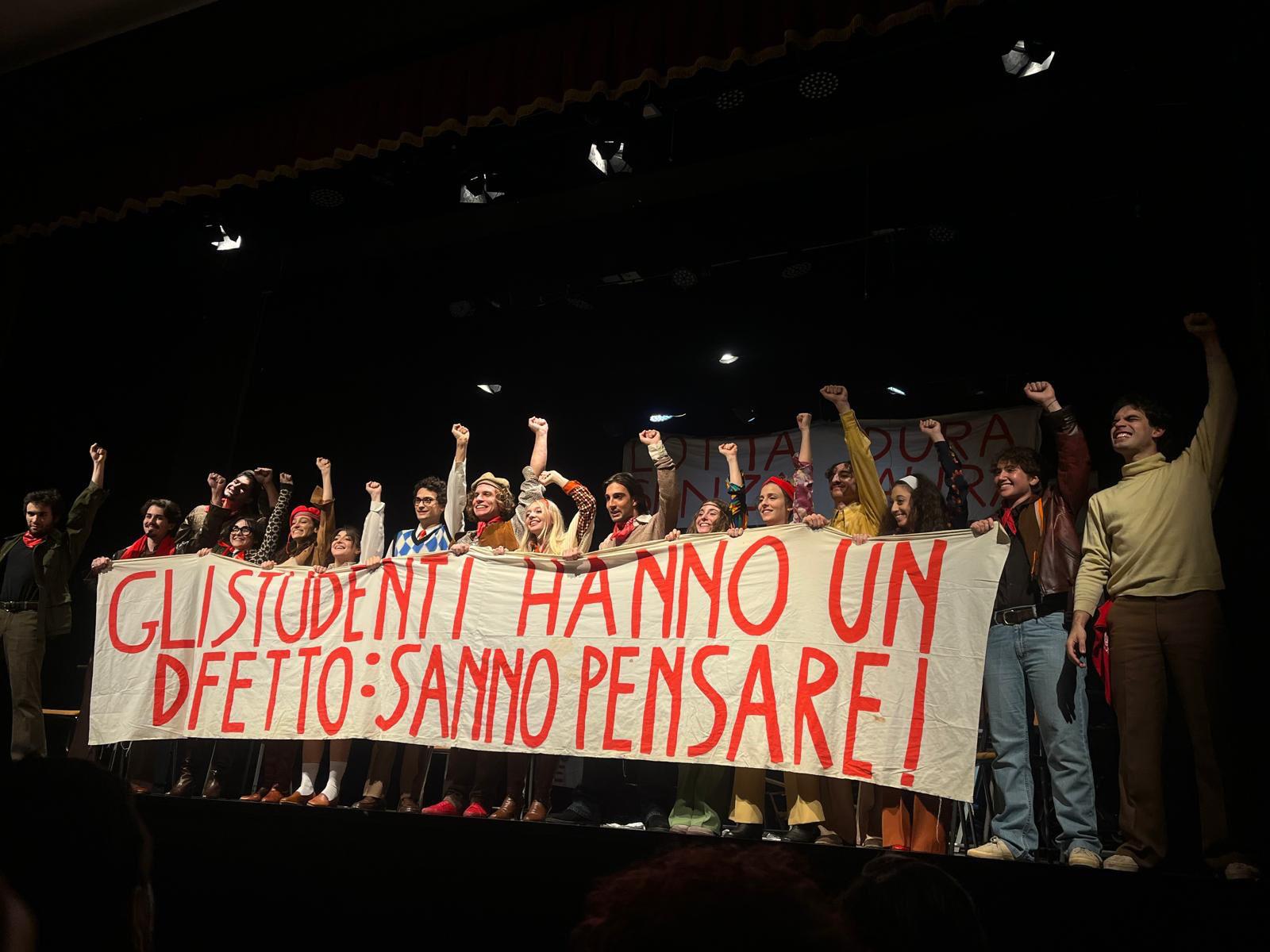 Il cast è in scena esibendo uno striscione di protesta