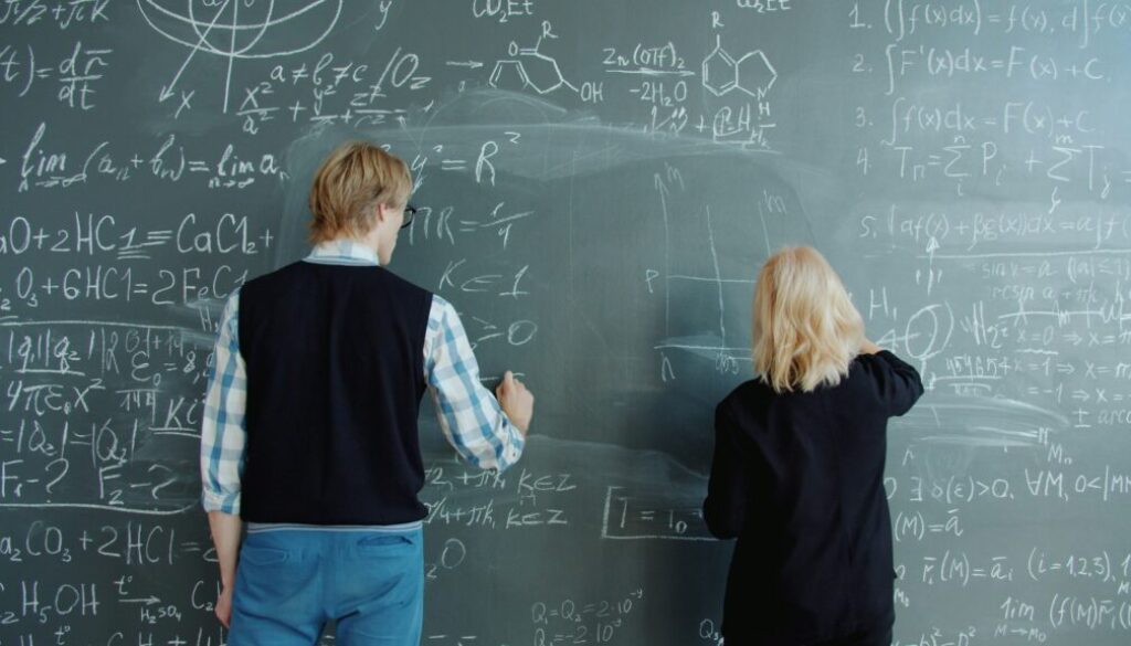 Due ragazzi giovani scrivono alla lavagna delle formule matematiche.