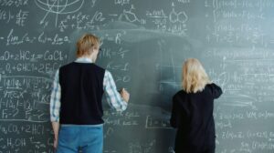 Due ragazzi giovani scrivono alla lavagna delle formule matematiche.