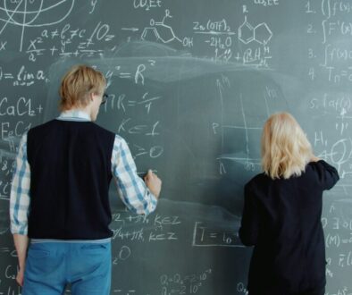 Due ragazzi giovani scrivono alla lavagna delle formule matematiche.