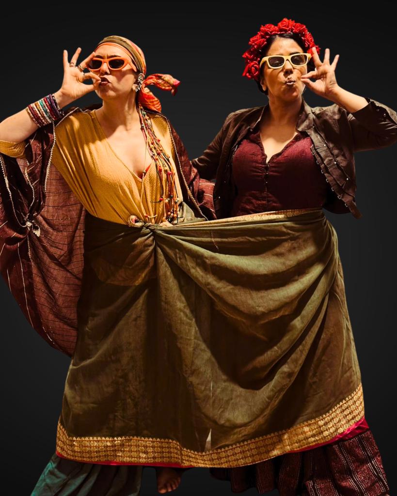 Taranjit Kaur e Dilnaz Irani in Chai Queens - le due attrici sono abbigliate con abiti quasi zingareschi e imitano l'azione di bere il tè